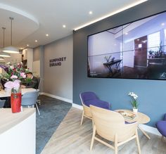 an office lobby with blue chairs and a large television mounted to the wall above it