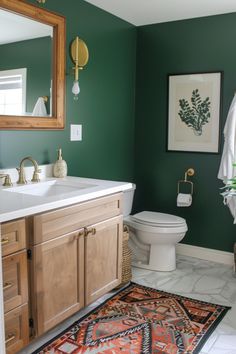 a bathroom with green walls and white counter tops, wooden cabinetry, and rug on the floor