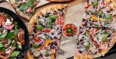 two pizzas with different toppings are on a cutting board next to a bowl of salad