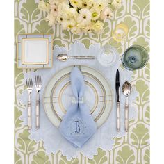 a place setting with silverware, napkins, and flowers on a green wallpapered tablecloth