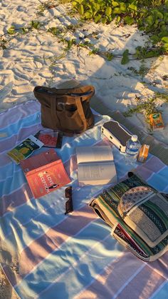 an open book and other items are laying on a blanket at the beach near a bag