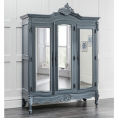 an ornate blue armoire with mirrored doors and mirrors on the front, in a white room