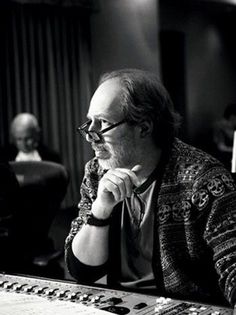 a man sitting at a mixing desk in front of a microphone and sound board with other people behind him