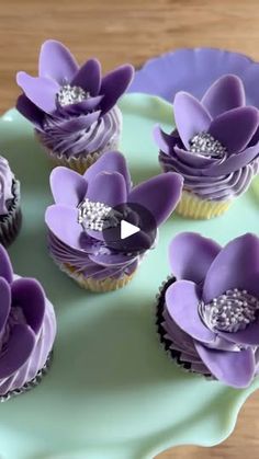 cupcakes with purple icing and flowers on a green plate that is sitting on a wooden table