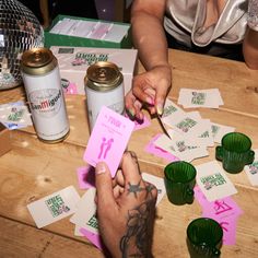 two people cutting up pink paper on top of a wooden table next to cans and cups