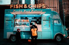 a man and woman standing in front of a blue food truck with neon signs on it