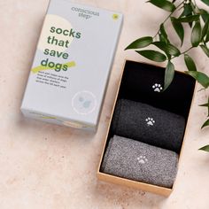 two socks in a box next to a plant on a table with a card board that says socks that save dogs