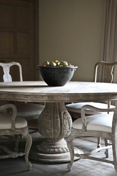 a bowl of fruit sitting on top of a table next to two chairs in front of a window