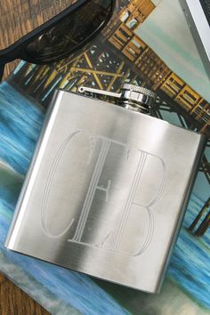 a stainless steel flask with the letter b on it next to sunglasses and a book