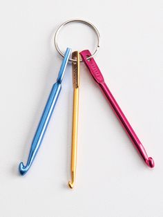 three different colored metal items on a white surface, one has a keychain and the other is a pen