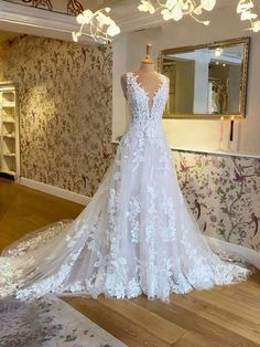 a white wedding dress on display in a room with floral wallpaper and wooden flooring