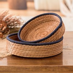 two woven baskets sitting on top of a wooden table next to a pine cone decoration