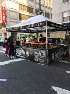 an outdoor food stand on the side of the road with people standing around it and eating