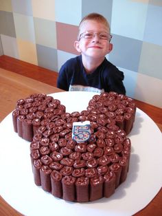 a young boy sitting in front of a mickey mouse cake with chocolate frosting on it