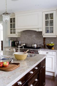 a kitchen with white cabinets and marble counter tops, an island in the middle has fruit on it