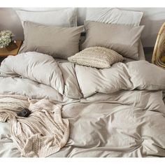 an unmade bed with several pillows and blankets on it, next to a wicker basket