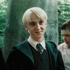 a young boy in a harry potter outfit standing next to two other boys wearing white shirts and green ties