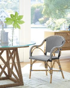 a wicker chair next to a table with a vase on it and a window in the background