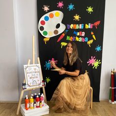 a woman sitting on a chair in front of a blackboard with paint and crayons