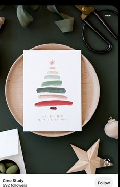 a christmas tree card sitting on top of a wooden plate next to other holiday decorations