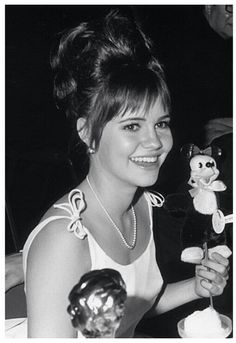 a woman sitting at a table with a cake in front of her and an owl figurine next to her