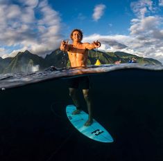 a man standing on a surfboard in the middle of the ocean with his thumbs up