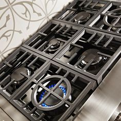 the gas stove has four burners and is stainless steel with blue flames on it