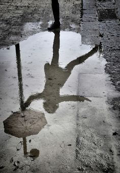 a person is standing in the rain with an umbrella reflected in it's puddle