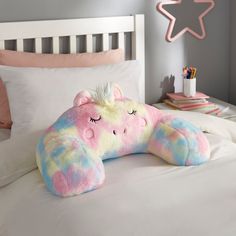 a pink and blue stuffed animal laying on top of a bed next to a white pillow