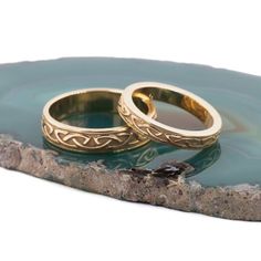 two gold wedding rings sitting on top of a rock