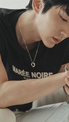 a young man holding a cell phone while wearing a black shirt with writing on it