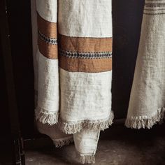 a pair of white towels hanging from the side of a door with tassels on them