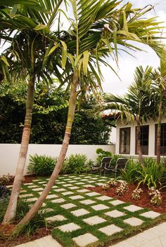 a white house surrounded by lush green trees and plants in front of the door is a small patio with two chairs on it