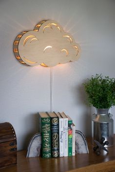 a wooden cloud shaped light sitting on top of a book shelf next to a potted plant