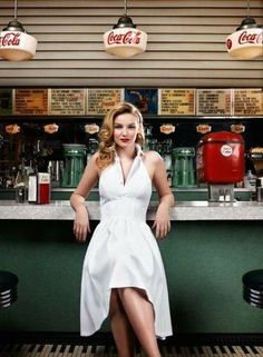 a woman in a white dress sitting at a bar