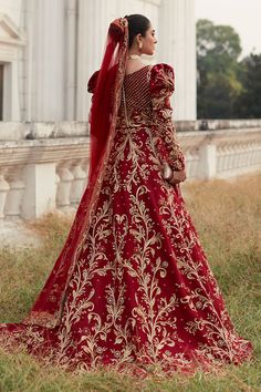 a woman in a red and gold wedding gown standing on the grass near a building