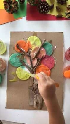 a young child is painting an autumn tree with acrylic paint on cardboard paper