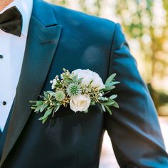 a man in a tuxedo wearing a boutonniere with white flowers and greenery