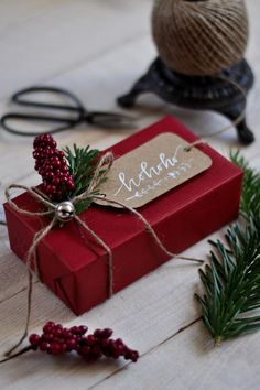 a red box with a tag tied to it sitting on a table next to some pine branches