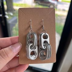 a pair of silver earrings sitting on top of a piece of cardboard next to a window