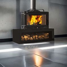 a black stove with logs in it on the floor next to a wall and windows