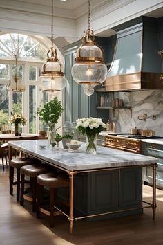 a kitchen with blue cabinets and marble counter tops, gold pendant lights over the island