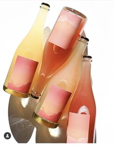 three wine bottles sitting next to each other in front of a white background with pink and yellow labels