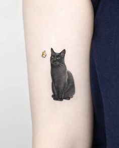 a small black cat with a tiny yellow flower on its left arm, sitting next to it's tail