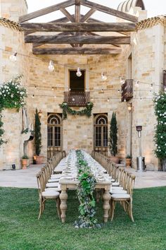 a long table with white chairs and greenery is set up in front of an old stone building