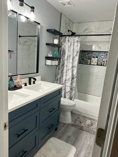 a bathroom with gray and white walls, wood floors and blue cabinetry in the shower area