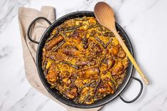 a skillet filled with food next to a wooden spoon on top of a table