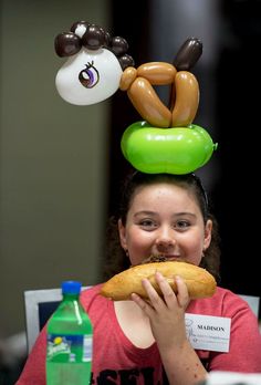 a woman sitting at a table eating a doughnut with balloons on top of her head