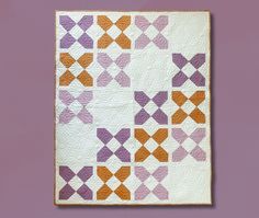 an orange and purple quilt hanging on a wall