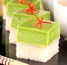 three pieces of green and white dessert sitting on top of a black table next to a cup